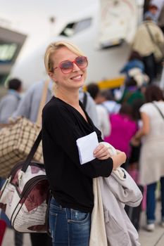 Joyful woman holding carry on luggage queuing to board the commercial airplane.