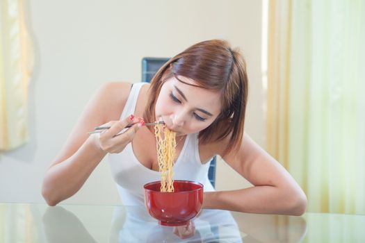 Young Asian girl eating ramen noodles using chopsticks