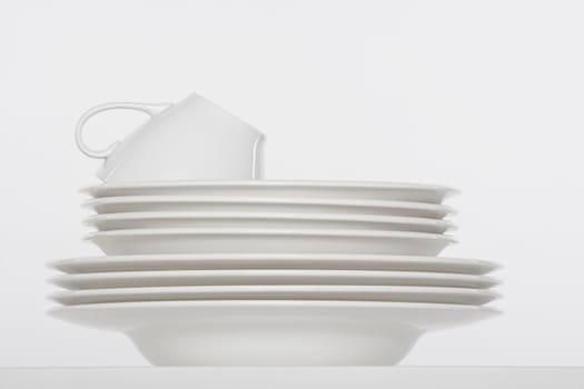 studio shot of a pile of white plates and white cup isolated on white