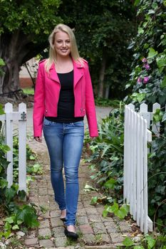 Beautiful young blond woman in pink jacket standing at a gate outdoors