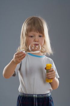 boy with long blond hair looking at big soap bubble - isolated on gray