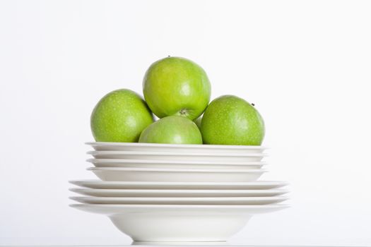 studio shot of a pile of plates and green apples isolated on white