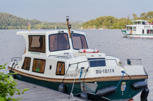 Essen, Germany - June 21.2014: Free license charter boat houseboat the Green fleet moored on the Baldeneysee in Essen. The Green Fleet rented various unlicensed charter boats. In the background, the passenger vessel Steele.