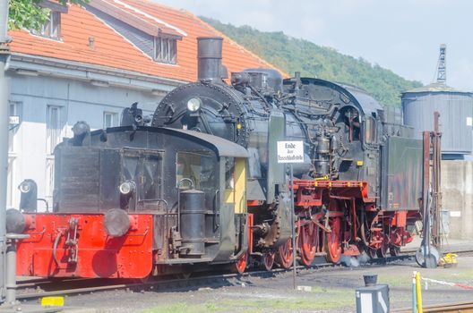 Exit and back view of a steam locomotive under full steam at the exit of a train station.