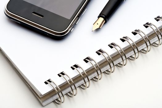 extreme closeup of a fountain pen, spiral notebook and cell phone