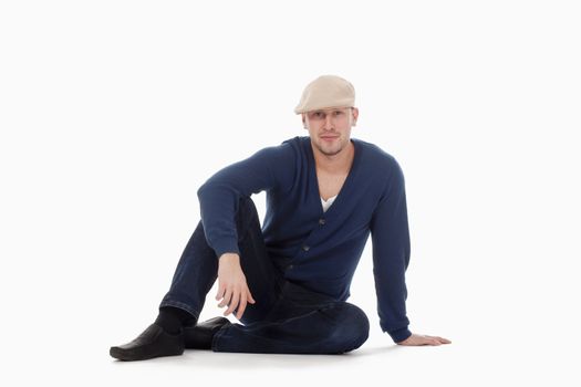 young handsome man with cap, sitting on the floor isolated on white