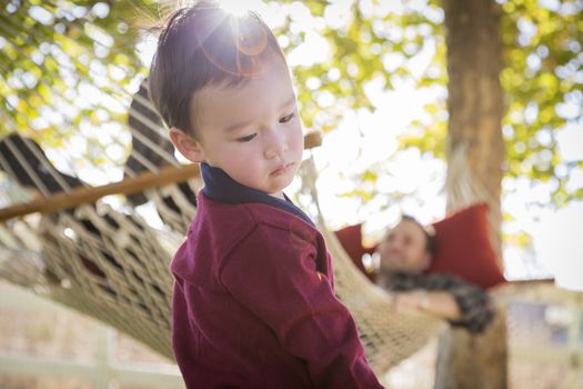 Mixed Race Boy Having Fun Outside While Parent Watches From Behind in a Hammock.