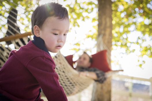 Mixed Race Boy Having Fun Outside While Parent Watches From Behind in a Hammock.