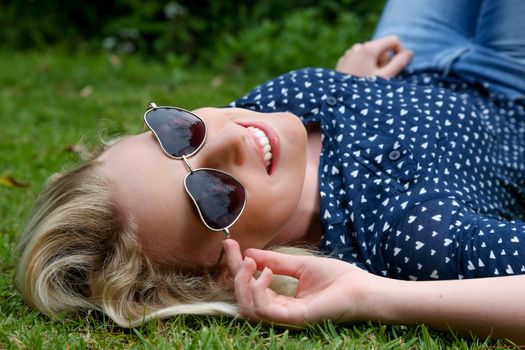 Lovely young lady relaxing on the grass and wearing heart shaped sunglasses