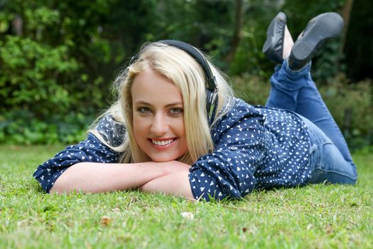Lovely young lady relaxing on the grass and listening to music on earphones