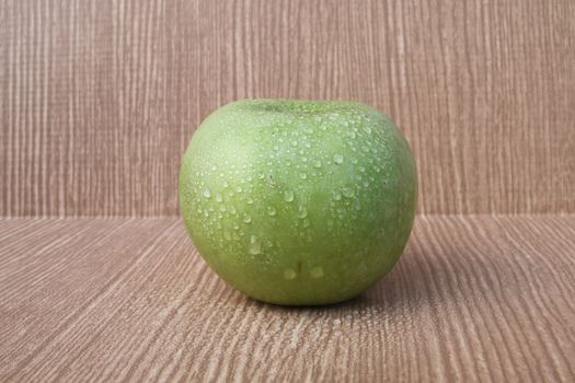 green apple on wooden background with some drops.