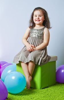 Little girl sitting on cube over gray background