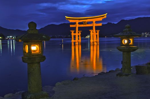 Great floating gate (O-Torii) on Miyajima island near Itsukushima shinto shrine, Japan shortly after the sunset with lit lanterns on the shore