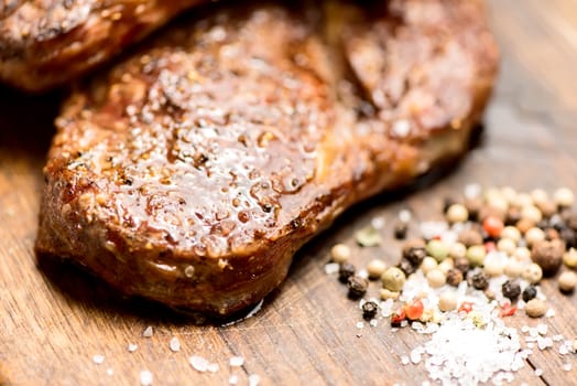 Succulent thick juicy portions of grilled steaks on an old wooden board with salt and pepper