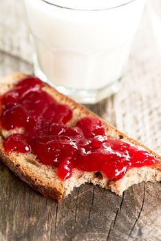 Bread with strawberry jam and glass of milk on wooden table