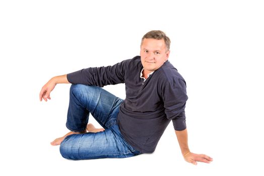 Casually dressed middle aged man barefoot sitting on a floor. Man shot in horizontal format isolated on white.