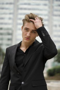 Handsome blond young man outdoor in city setting, touching hair with his hand, in business suit