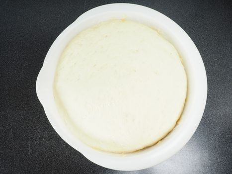 Proven dough in a white plastic bowl on black table