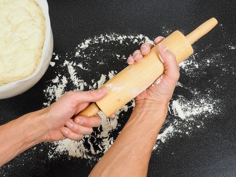 Person preparing a wooden rolling pin with wheat flour before working with the dough