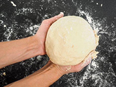 Person holding a proven dough over black table with flour mess