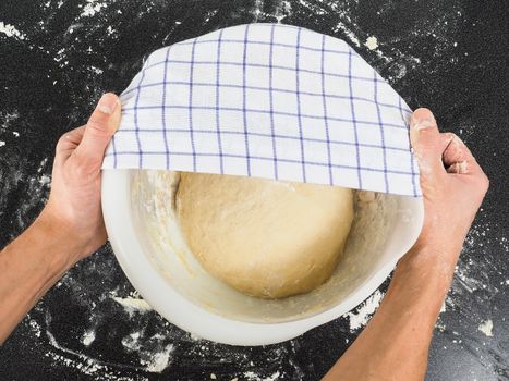 Person covering a dough for proving in a bowl on black table