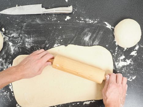 Person handling a dough with a rolling pin floured black table