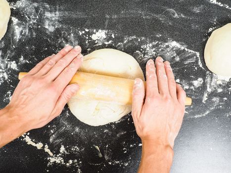 Person handling a dough with a rolling pin floured black table