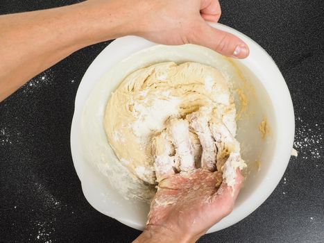 Person kneading a sticky dough in white bowl on black table