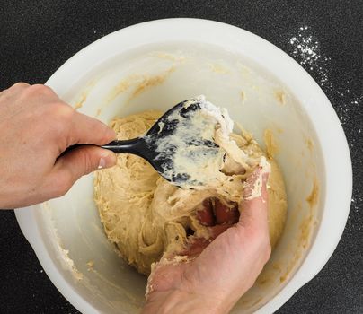 Person handling a sticky dough with black spatula in white plastic bowl on black table