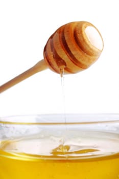 Honey dripping from a wooden dipper in glass bowl.