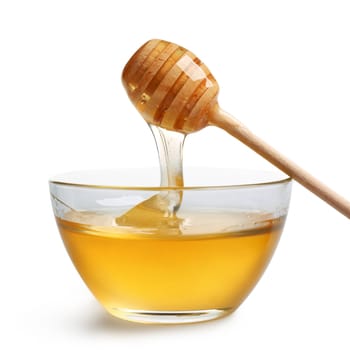 Honey dripping from a wooden dipper in glass bowl.