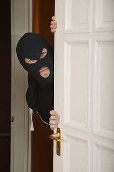 Robber in a black mask sneaking inside