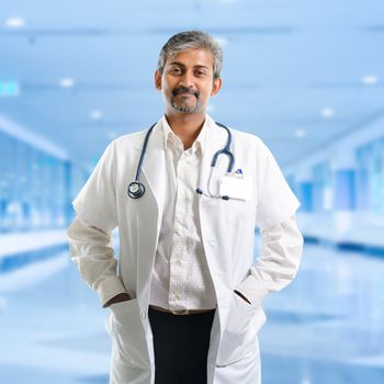  Mature Indian male medical doctor standing inside hospital. Handsome Indian model portrait.
