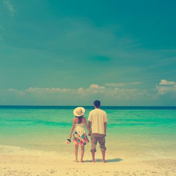 Rear view of couple holding hands walking at beach, in vintage style filter.