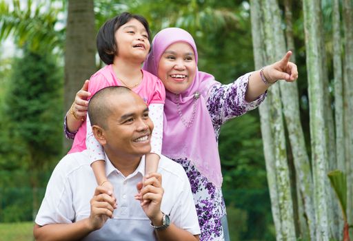 Happy Southeast Asian Muslim family pointing away, outdoor lifestyle at nature green park.