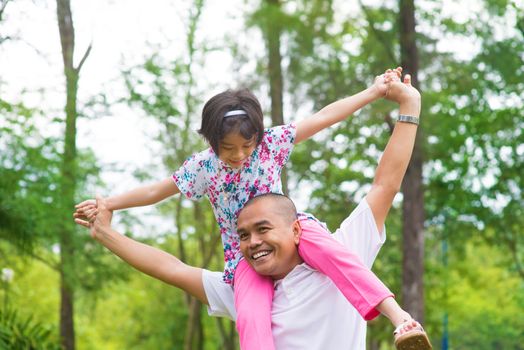 Father and daughter playing piggy back at outdoor garden park. Happy Southeast Asian family living lifestyle.