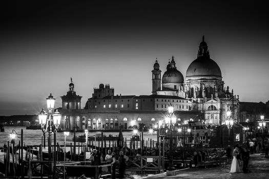 Romantic Italian city of Venice in black and white. World Heritage Site. Traditional Venetian wooden boats, gondolier and Roman Catholic church Basilica di Santa Maria della Salute.