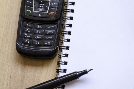 Blank notebook and ink pen on a wooden desk and old phone