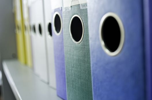 Red, green, blue and yellow office folders with boxes on the gray shelf