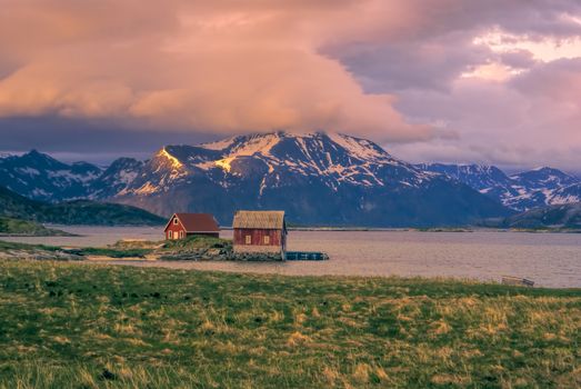 Picturesque view of two red wooden houses standing on the shore on Sommaroy