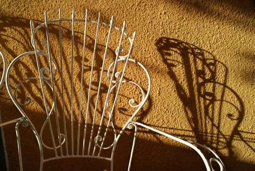 Picturesque view of a white garden chair casting a shadow on terracotta wall
