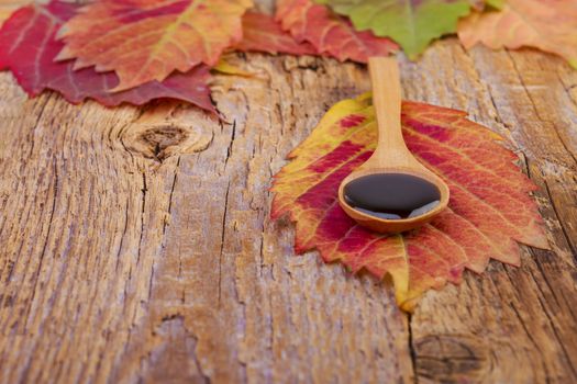 leaf and syrup in wooden spoon on wooden background