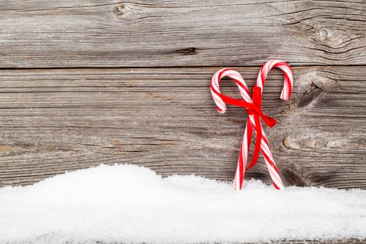 Colorful striped red and white Xmas candy canes with winter snow on wooden boards, with copyspace