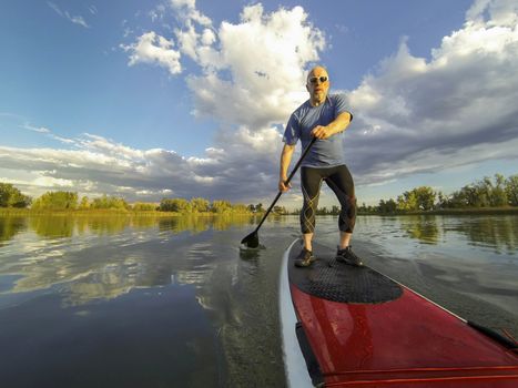 senior male paddler enjoying workout on stand up paddleboard (SUP), calm lake in Colorado, summer