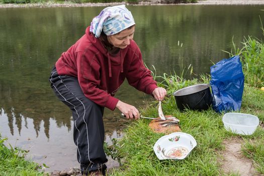 A woman cleans a fish on the river bank