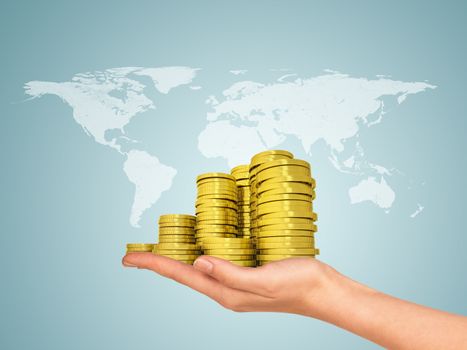 Female hand holding stack of gold coins. World map on background