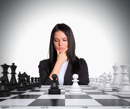 Lost in thought businesswoman looking at chess board with chess. Gray background. Business concept