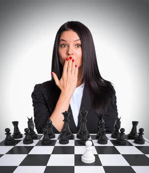 Surprised businesswoman looking at camera. Chessboard with chess. Gray background. Business concept