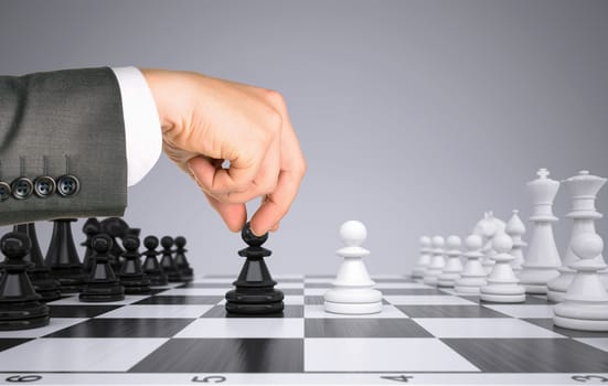 Businessman hand touching king pawn on chess board. Gray background. Business concept