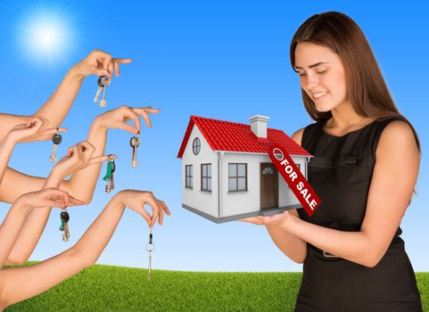Beautiful smiling girl holding house with label. Many hands are given keys. Grass and sky in background